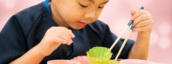子どもが箸で容器の中身をつかもうとする様子