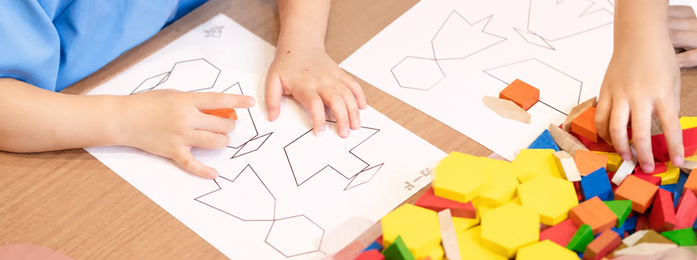 紙の図形に色付きブロックを置く子どもの手元
