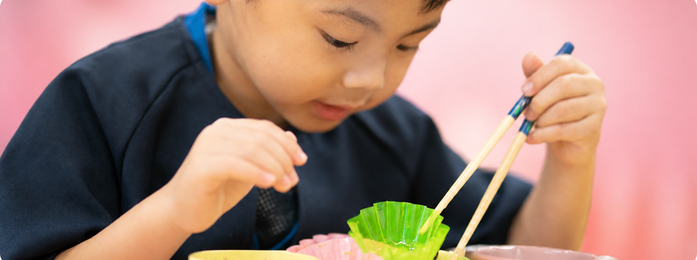 子どもが箸で容器の中身をつかもうとする様子