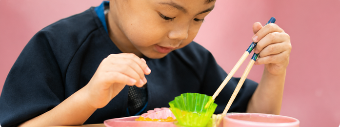子どもが箸で容器の中身をつかもうとする様子