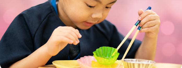 子どもが箸で容器の中身をつかもうとする様子