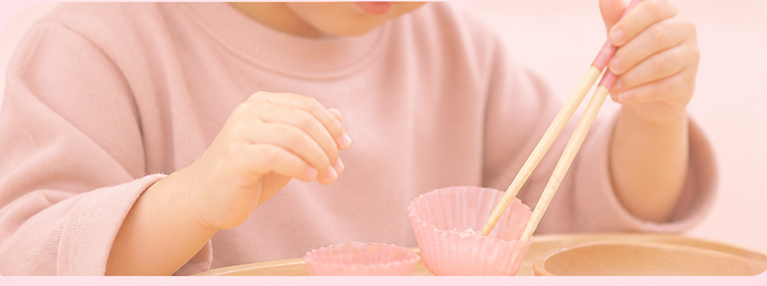 子どもが箸で容器の中のものをつかむ写真