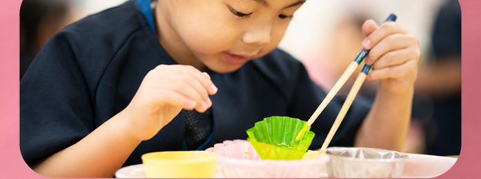 子どもが箸で容器の中身をつかもうとする様子