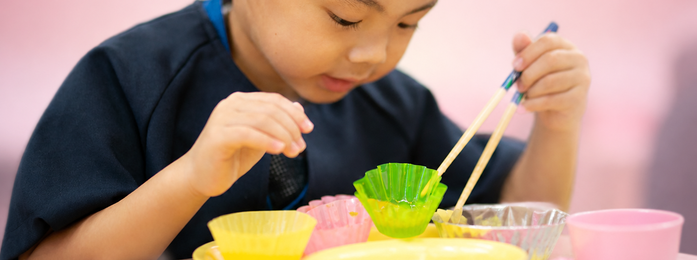 子どもが箸で容器の中身をつかもうとする様子