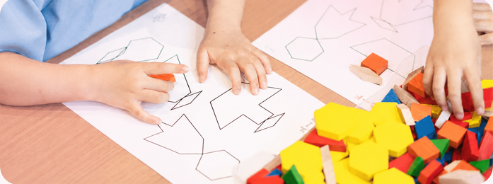 紙の図形に色付きブロックを置く子どもの手元